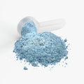 Blue powder spilling out of a white scoop on a light gray background