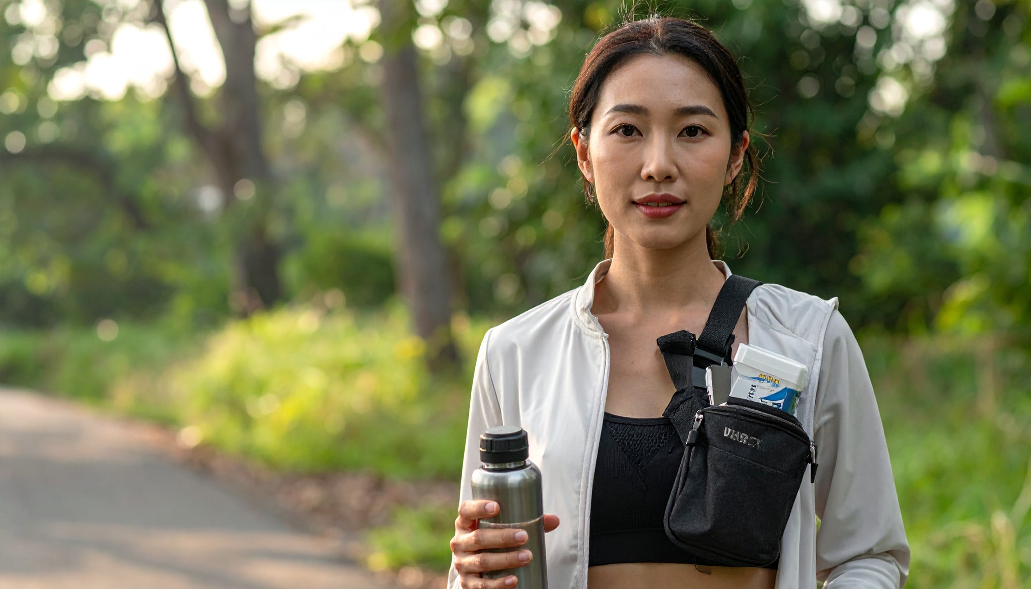 Woman holding a water bottle and a small bag outdoors