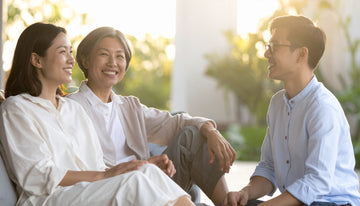 Three people sitting together outdoors, smiling and enjoying each other's company.